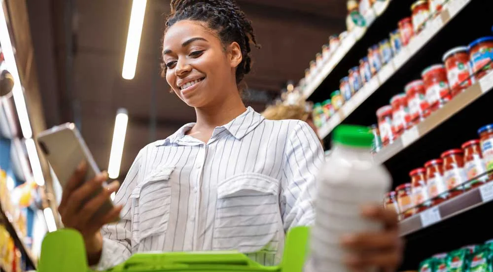Sem Parar Empresas: mulher em supermercado olhando seu celular para conferir os saldos dos benefícios flexíveis para pagamento da compra