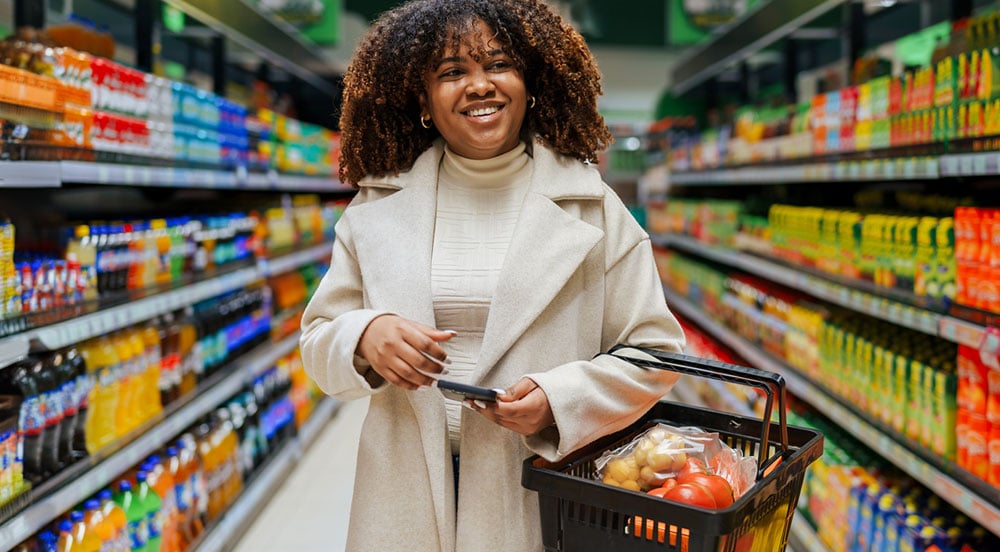 Sem Parar Empresas: mulher em supermercado com cestinha cheia de compras no braço, certificando-se se o vale-alimentação é obrigatório