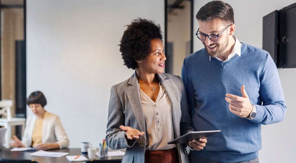 Sem Parar Empresas: homem e mulher em escritório com mais pessoas ao fundo conversando sobre quando o funcionário não tem direito a vale-transporte