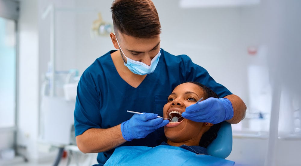 Dentista examinando a saúde bucal de uma mulher que utiliza a assistência odontológica Sem Parar Empresas
