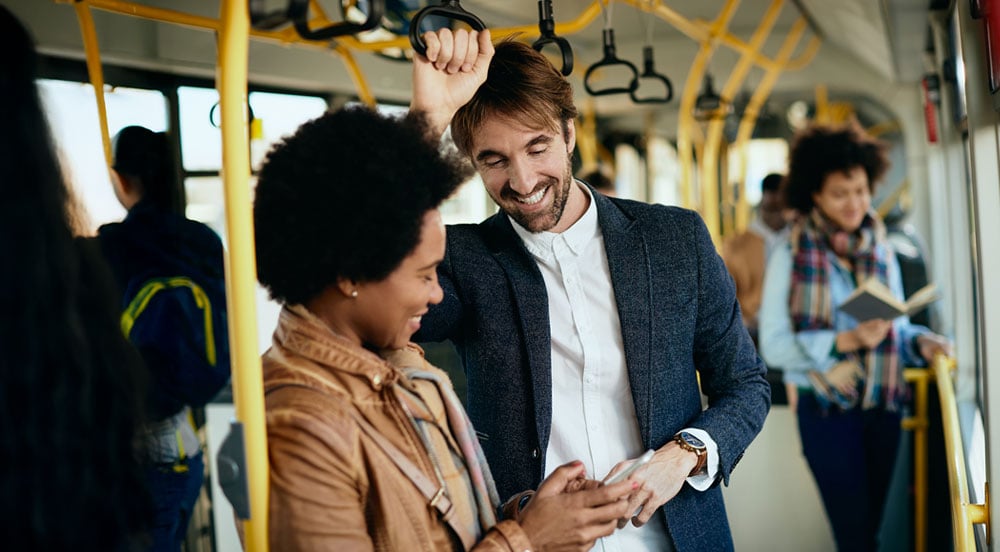 Alt text  Sem Parar Empresas: pessoas sorrindo no ônibus utilizando o celular para calcular o tempo de deslocamento para o trabalho
