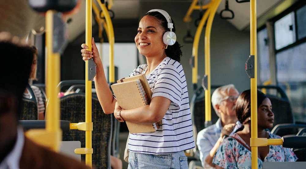 Sem Parar Empresas: Mulher jovem com fones de ouvido em um ônibus utilizando o vale-transporte para estagiários para ir até seu local de trabalho