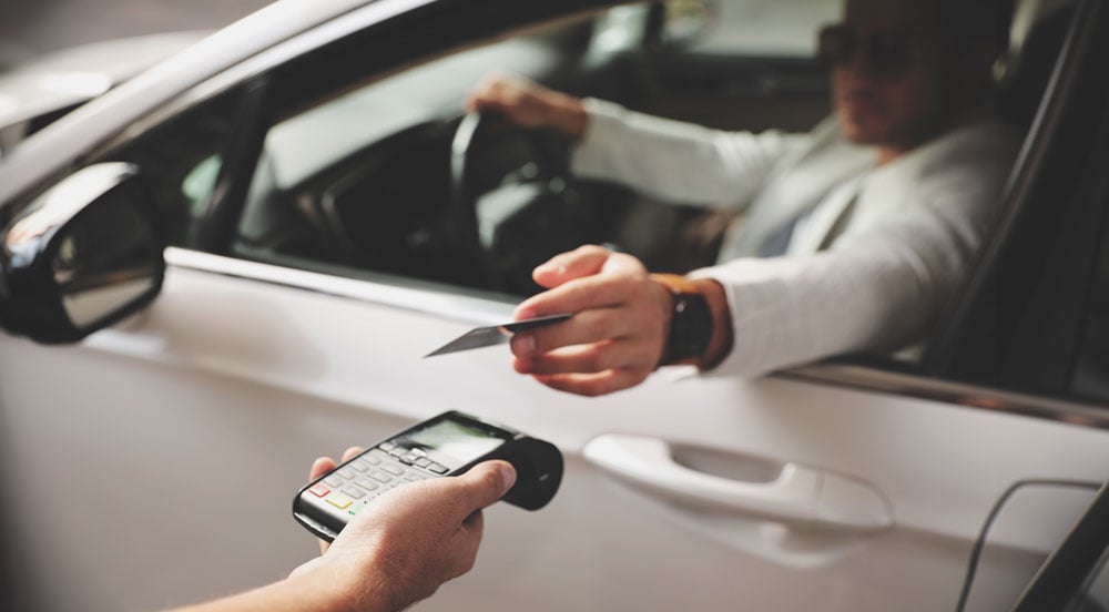 Homem em um carro aproximando a mão com o Cartão Auto Sem Parar Empresas a uma maquininha