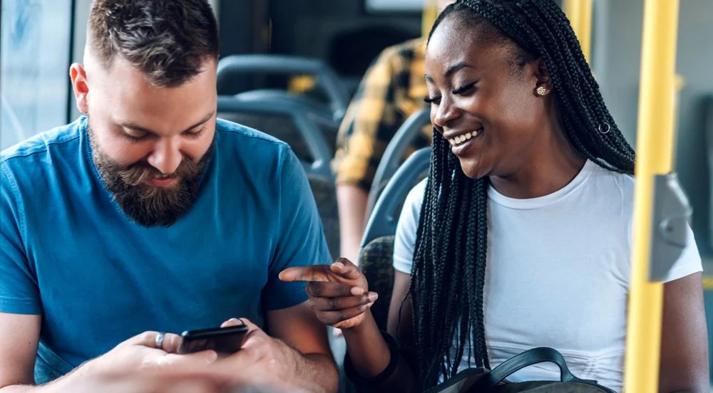 Homem e mulher sorrindo sentados em um ônibus, pois estão usando o auxílio-mobilidade da Sem Parar Empresas