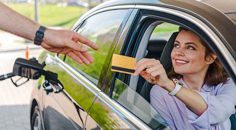 Sem Parar Empresas: mulher no carro entregando o cartão para o frentista do posto de combustível, ela está sorrindo representando que houve sucesso do cliente
