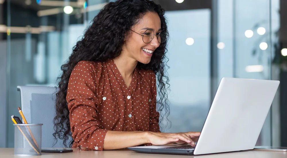 Mulher sorrindo olhando para a tela do notebook que está logado no CTF online da Sem Parar Empresas