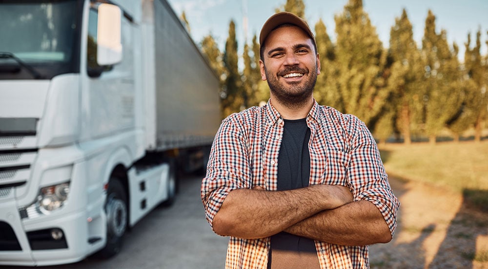 Sem Parar Empresas: motorista em frente ao veículo com braços cruzados e sorrindo porque sabe quanto ganha um caminhoneiro