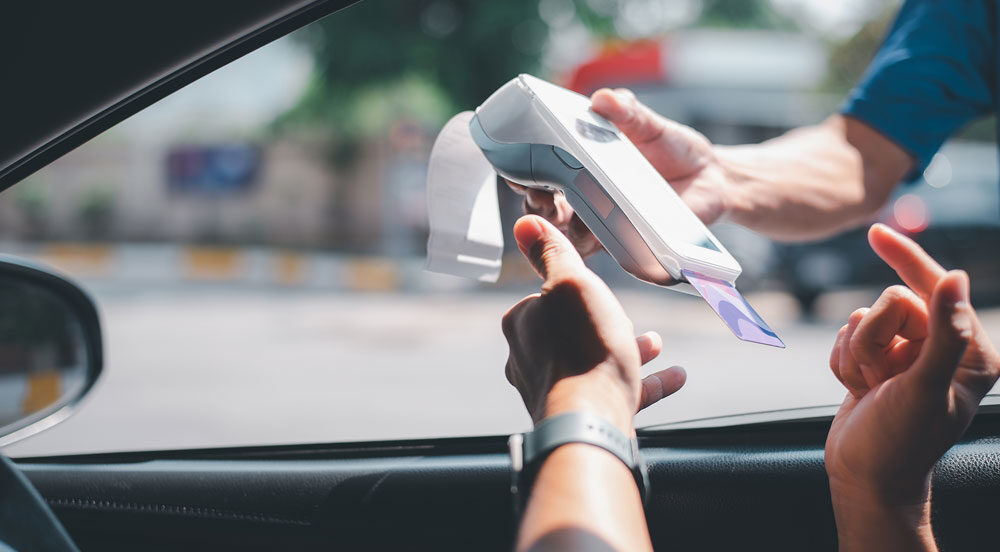 Pessoa dentro de um carro, recebendo uma maquininha do frentista para pagar pelo combustível com o cartão frota da Sem Parar Empresas