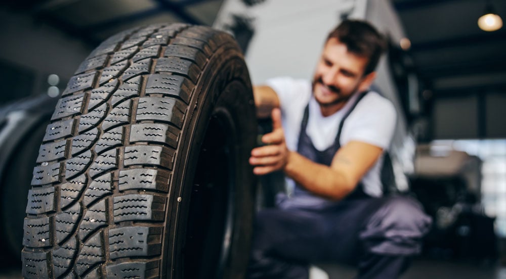 Sem Parar Empresas gestão de pneus de caminhão: pneu novo sendo segurado à frente com homem encaixando no veículo