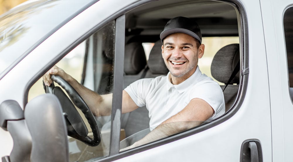 Motorista sorrindo dentro de uma vã, pois faz o uso da tag Sem Parar para CNPJ