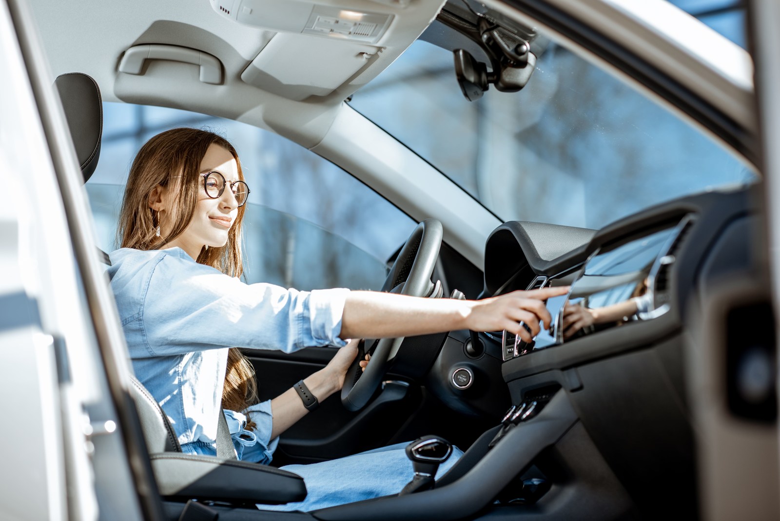 mulher sorrindo dentro de um carro enquanto troca a música do rádio