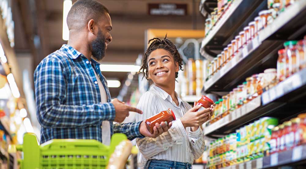 Homem e mulher em supermercado escolhendo produtos que entram no custo do vale-alimentação da Sem Parar Empresas