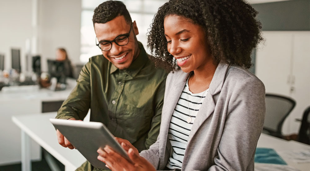 Sem Parar Empresas: homem e mulher sorrindo olhando o plano benefícios de empresas para funcionários​ em um tablet