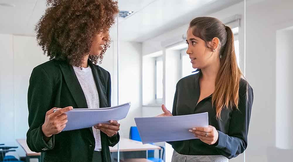 Sem Parar Empresas: duas mulheres em empresa conversando com papéis na mão que são os assessment