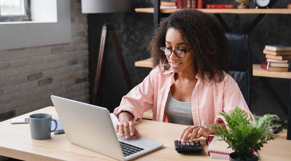 Sem Parar Empresas: mulher em frente ao computador usando a calculadora ao lado para entender o banco de horas dos funcionários