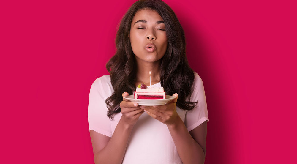 Sem Parar Empresas: mulher com um pedaço de bolo na mão, soprando sua vela no day off de aniversário fornecido pela empresa