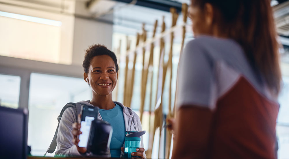 Sem Parar Empresas: mulher mostrando o celular na recepção onde tem desconto em academia