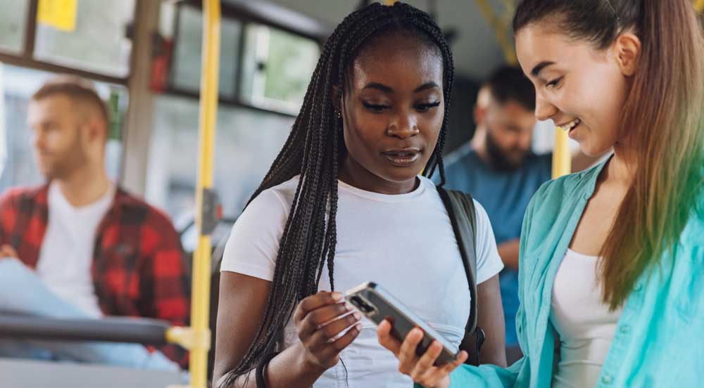 Duas mulheres no ônibus conferindo com o celular o Poupador Sem Parar Empresas