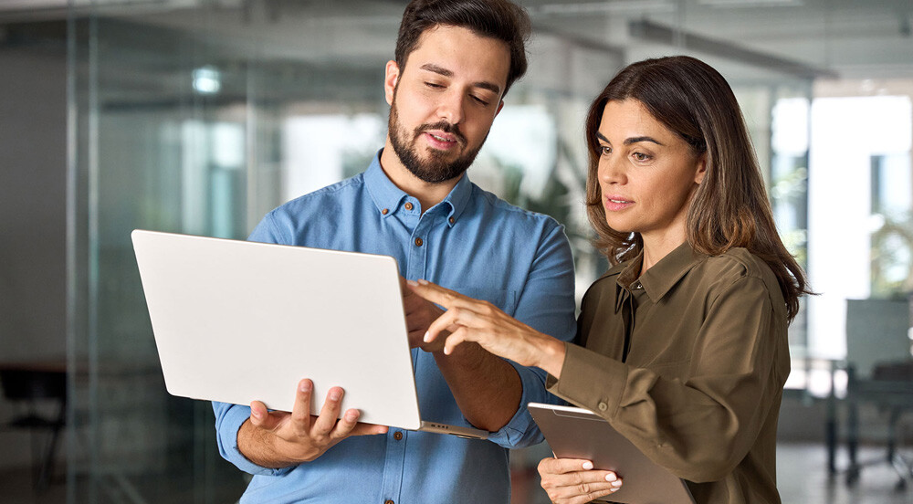 Homem e mulher em escritório olhando para tela de notebook para discutir sobre como acelerar os processos do RH com a Sem Parar Empresas