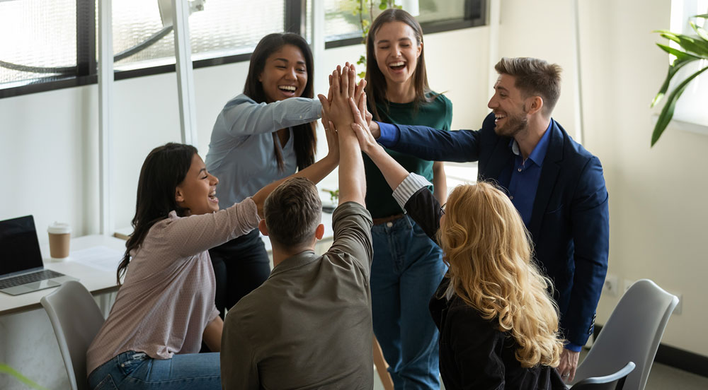 Sem Parar Empresas: seis pessoas unindo as mãos ao centro, dentro de um escritório que trabalha para a retenção de talentos