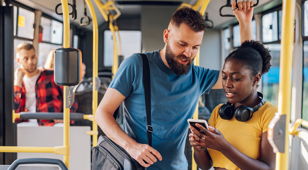 Sem Parar Empresas: um homem e uma mulher em pé em um ônibus olhando juntas para a tela do celular da moça para consultar se vale-transporte é obrigatório