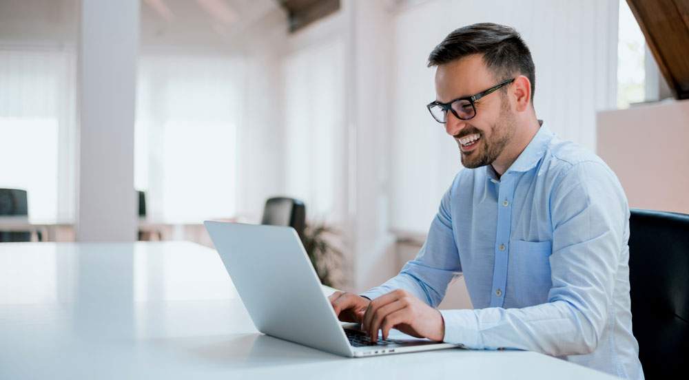 Sem Parar Empresas: homem sorrindo em frente a um computador, onde está realizando suas tarefas de RH