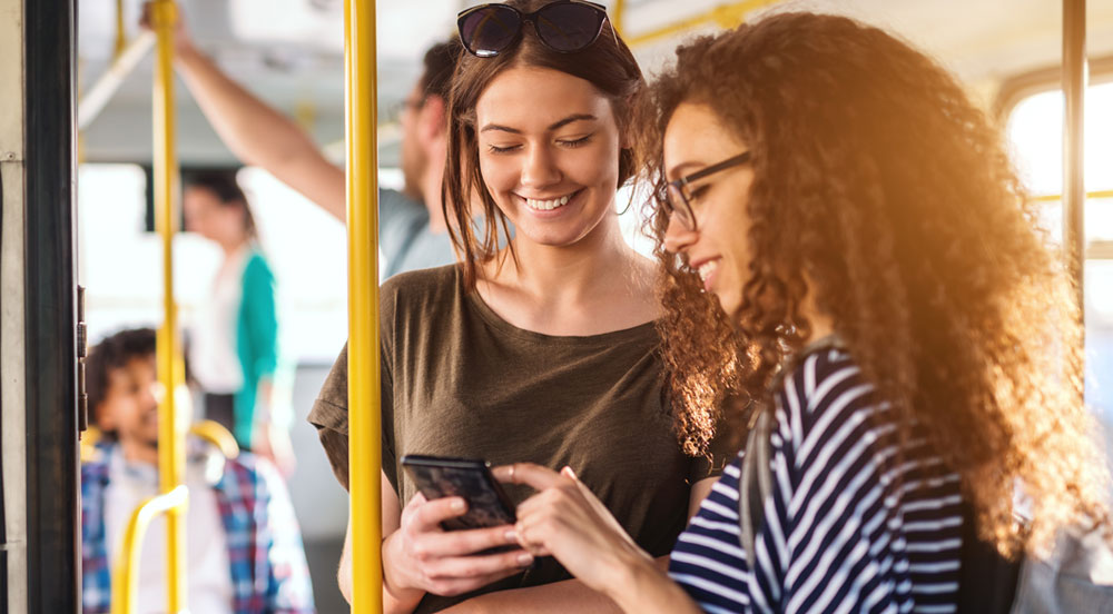 Duas mulheres em um ônibus olhando a tela de um celular e sorrindo porque possuem auxílio transporte da Sem Parar Empresas