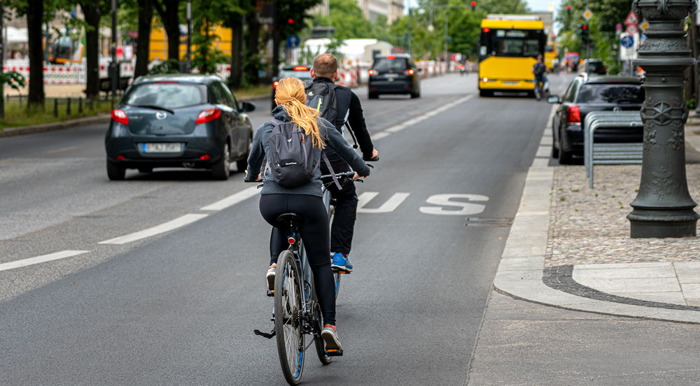Sem Parar Empresas: uma avenida com dois ciclistas, três carros e um ônibus, representando a mobilidade urbana