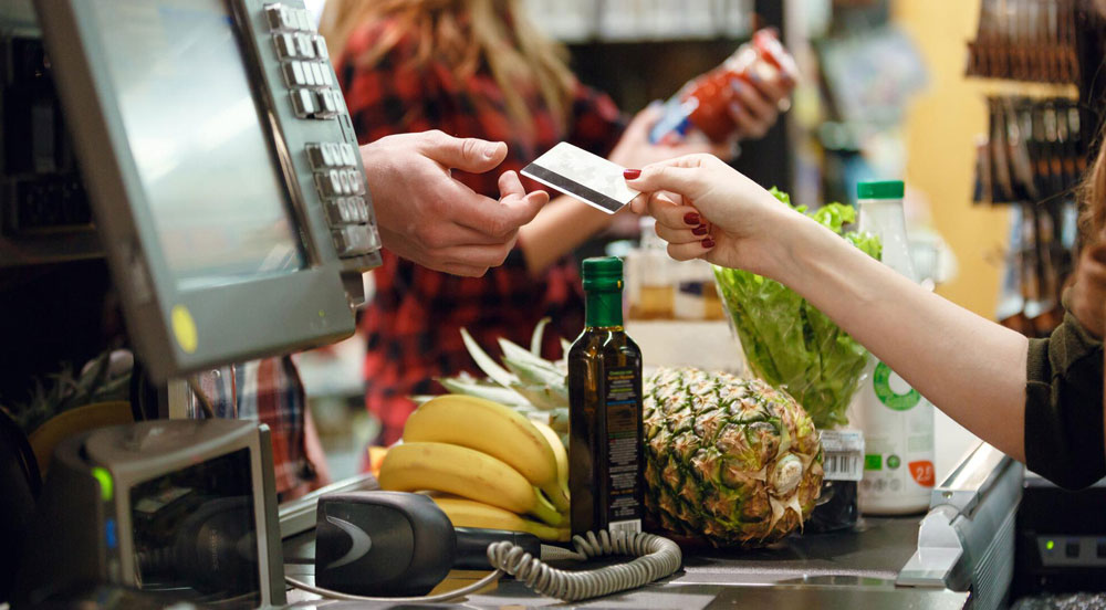Pessoa em caixa de supermercado usando os saldos do cartão FLEX Sem Parar Empresas para comprar frutas, azeite e verduras