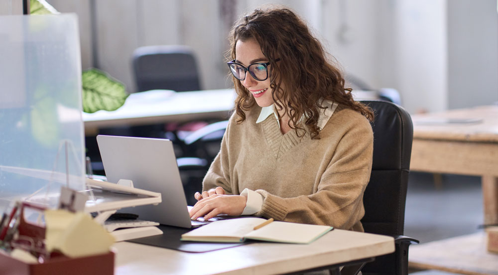 Mulher em um escritório olhando para a tela de um notebook que apresenta as soluções de benefícios Sem Parar Empresas