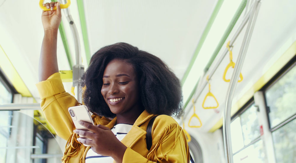 Mulher em transporte público sorrindo com um celular na mão, pois trabalha em local que faz a gestão do vale-transporte com a solução Sem Parar Empresas