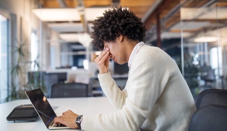 Sem Parar Empresas: homem em frente ao computador, com as mãos apertando os olhos, sinalizando que está tendo uma síndrome de burnout no ambiente de trabalho