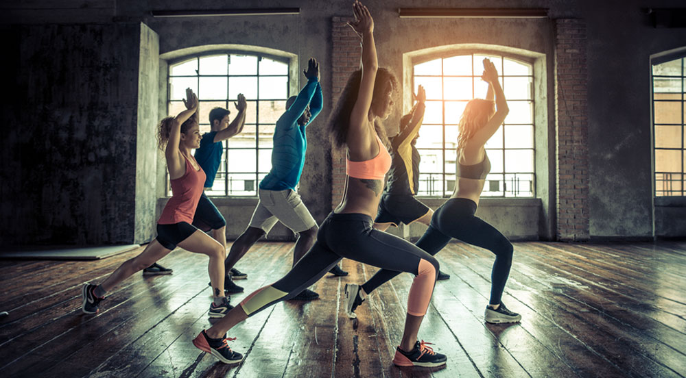 Seis pessoas de perfil fazendo um movimento de dança em uma sala de ginástica que aceita o Gympass Sem Parar Empresas como pagamento