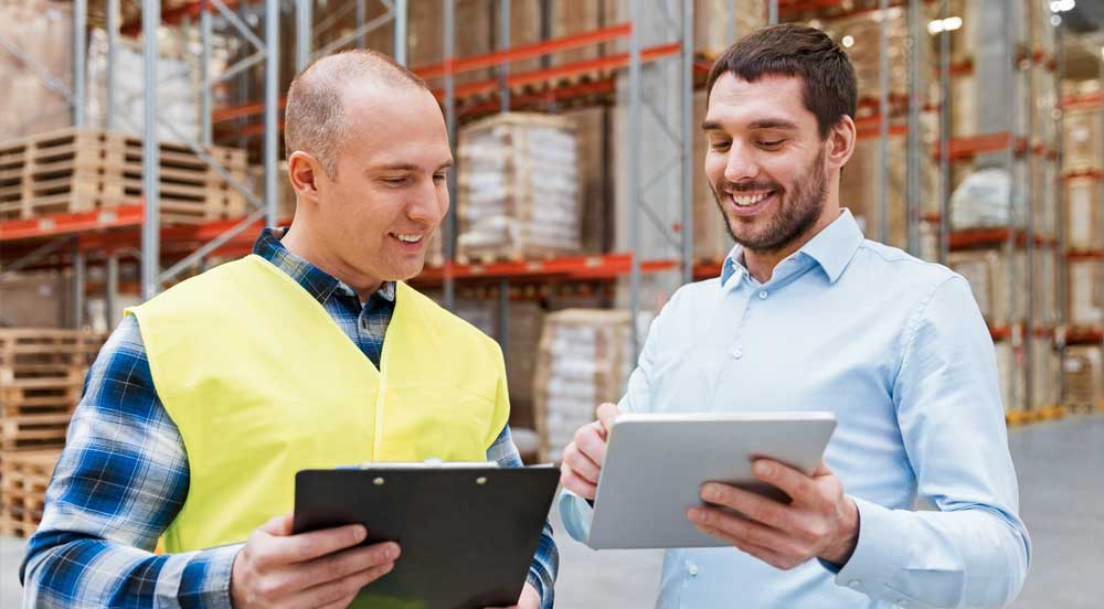 Sem Parar Empresas: dois homens em um armazém de logística fazendo o cálculo de impostos de forma automática em seus tablets