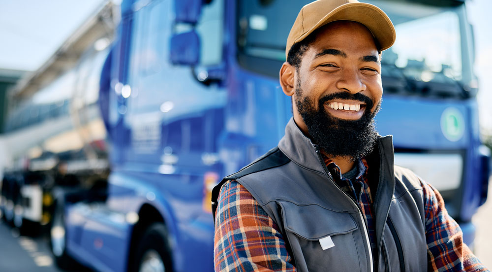 Sem Parar Empresas: homem sorrindo em frente a um caminhão azul, pois ele trabalha regulamentado com o CIOT