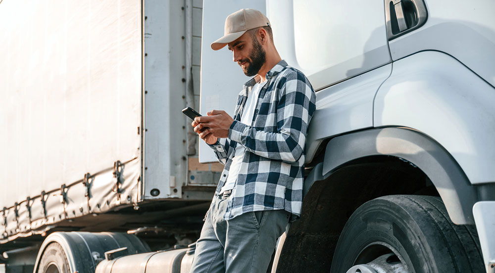 Homem encostado em caminhão branco, mexendo no celular para explorar o pagamento eletrônico de frete da Sem Parar Empresas