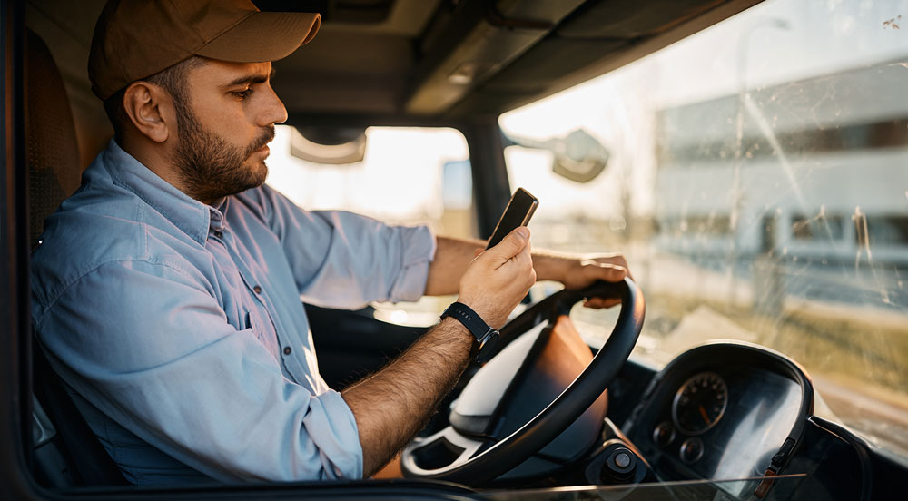 Homem dentro de um caminhão olhando para o celular para sacar o pagamento de frete no aplicativo Sem Parar Empresas