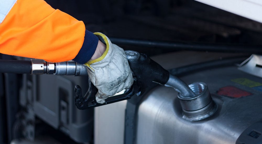 Mão inserindo bomba de combustível em tanque de caminhão que está abastecendo com cartão para abastecimento de frota da Sem Parar Empresas