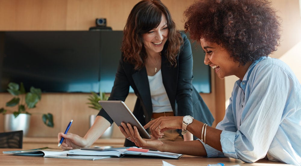 Duas mulheres do RH discutindo benefícios essenciais da Sem Parar Empresas. Elas utilizam tablet e cadernos para a gestão.