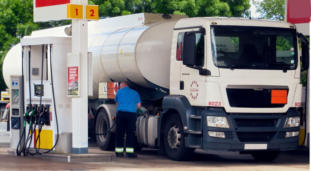 Caminhão branco em posto de combustível, onde o frentista está acoplando a mangueira de diesel para o controle de abastecimento de frota ser feito pelo gestor da transportadora. 
