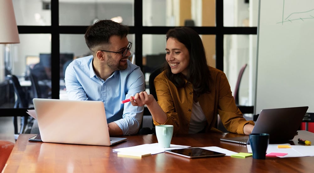 Mulher sentada em mesa de escritório conversando com um homem sobre o plano de benefícios Sem Parar Empresas