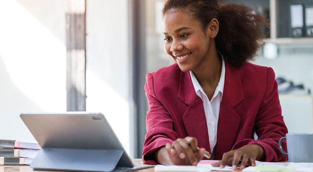 Mulher sorrindo em frente a um computador, com papéis e calculadora nas mãos para calcular o desconto do vale-transporte Sem Parar Empresas