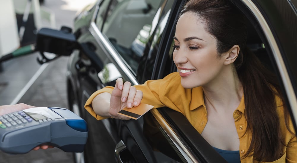 Mulher dentro de carro, abastecendo num posto de gasolina, passando o vale-combustível Sem Parar Empresas na maquininha de cartão