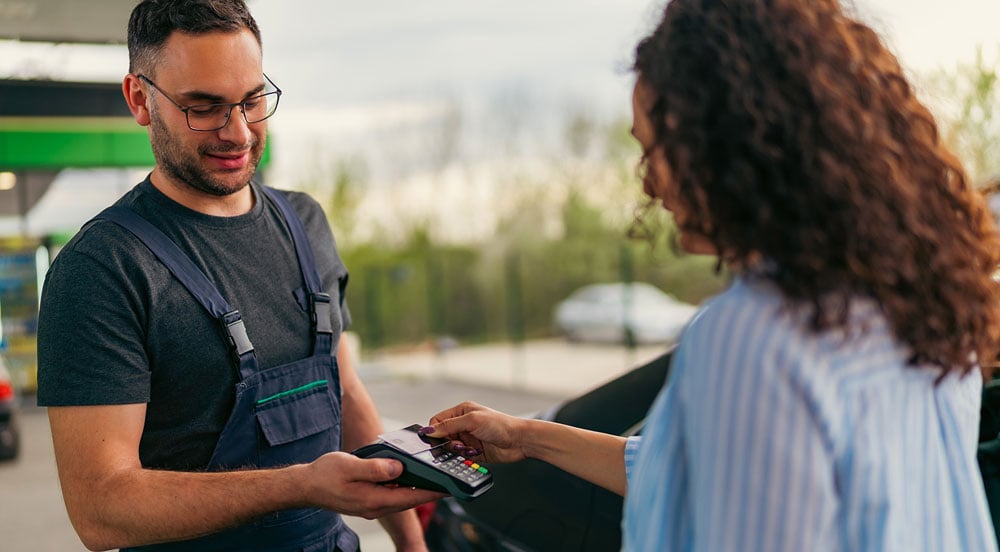 Mulher em posto de gasolina aproximando seu cartão combustível para empresas da Sem Parar Empresas à maquininha que está na mão do frentista