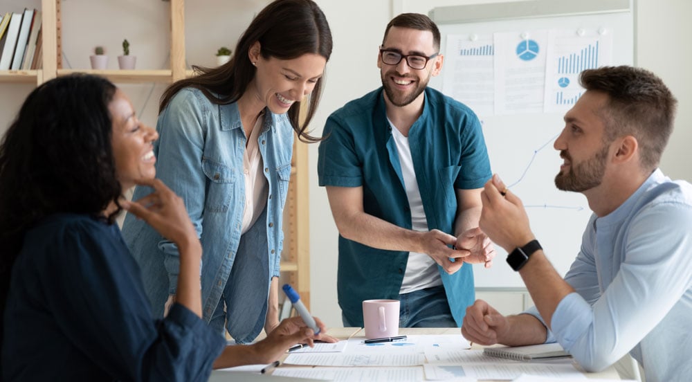 Sem Parar Empresas: quatro pessoas conversando em uma sala com mesa, lousa, papéis e livros, onde estão traçando estratégias de motivação para equipe 