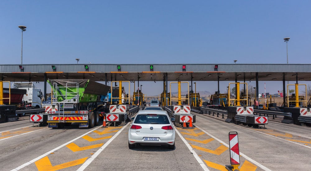 Caminhões e carros passando em praça de pedágio. Um deles, um carro corporativo que usa tag pedágio para MEI
