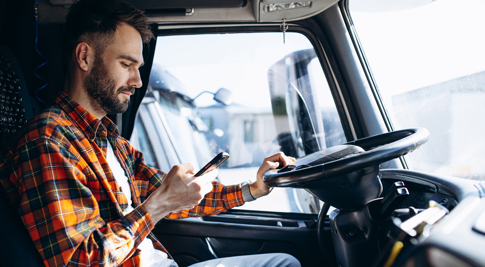 Sem Parar Empresas: caminhoneiro estacionado verificando o celular com contato à gestão de frete embarcador